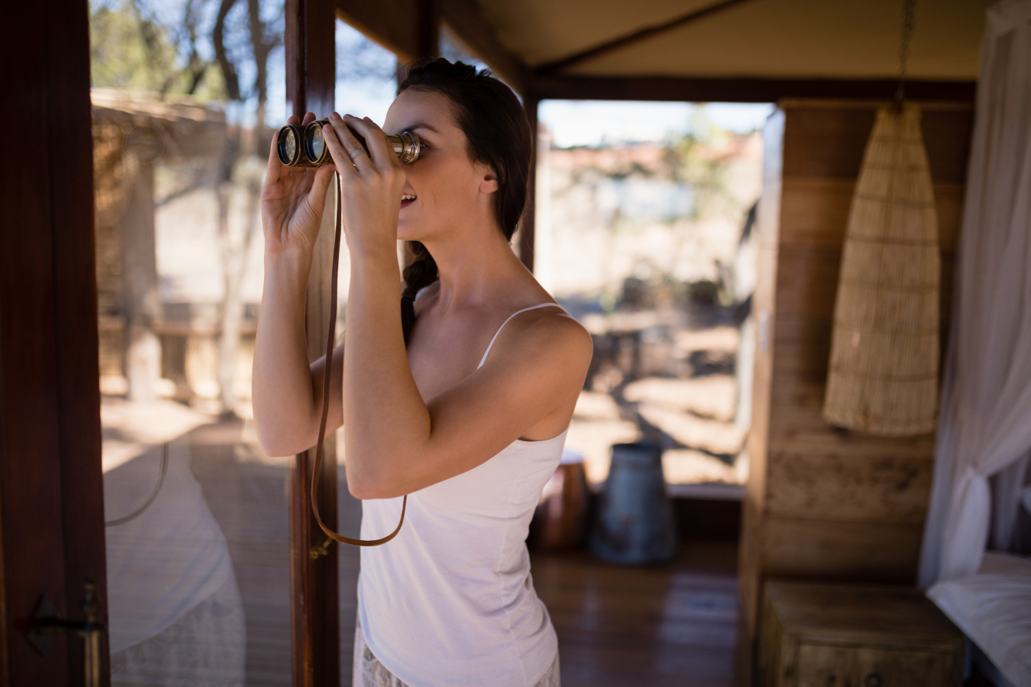 Belle femme regardant à travers des jumelles depuis la fenêtre